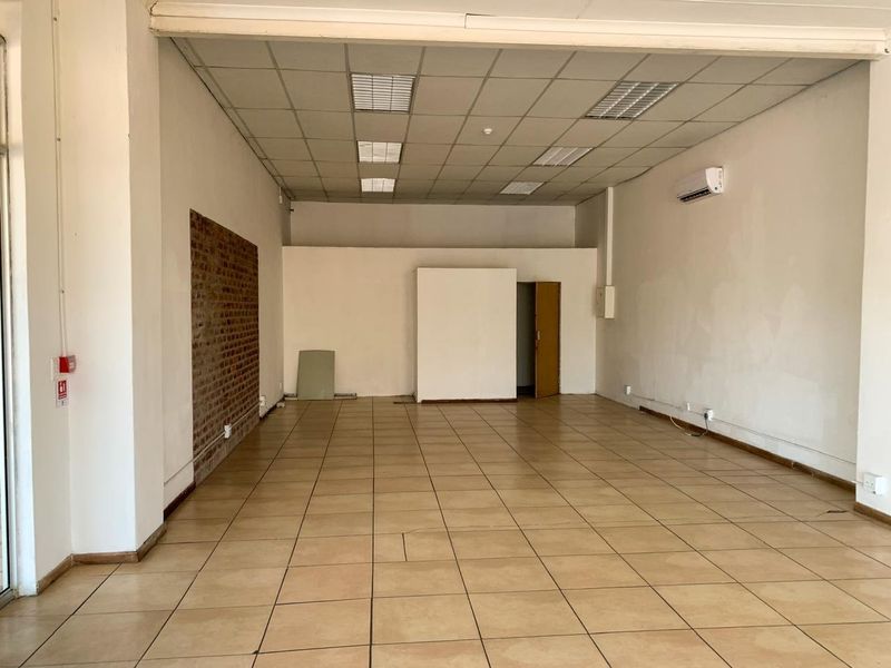 Open-plan commercial office space featuring ceramic tiled flooring, a suspended ceiling, and an exposed brick accent wall.