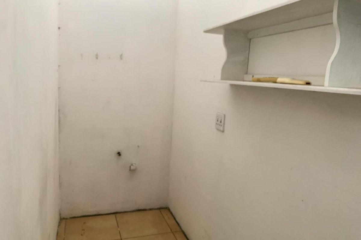 A small, empty utility space featuring tiled flooring, wall-mounted shelving, and an electrical outlet, suitable for storage or laundry conversion.