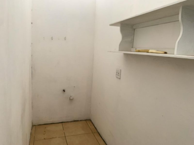 A small, empty utility space featuring tiled flooring, wall-mounted shelving, and an electrical outlet, suitable for storage or laundry conversion.