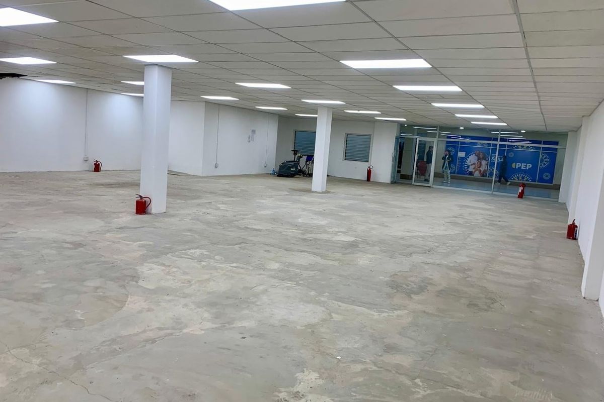 A large, open-plan commercial retail space featuring a suspended ceiling, recessed lighting, structural columns, and a glass storefront entrance.