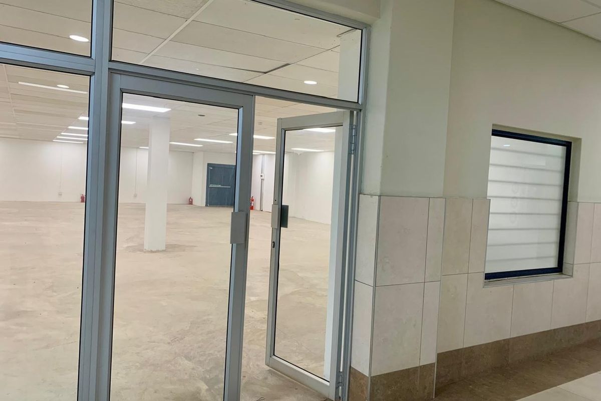 A spacious, vacant open-plan commercial unit featuring aluminium-framed glass entry doors, recessed ceiling lighting, and neutral tiled wall finishes.