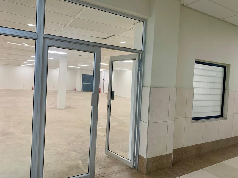 A spacious, vacant open-plan commercial unit featuring aluminium-framed glass entry doors, recessed ceiling lighting, and neutral tiled wall finishes.