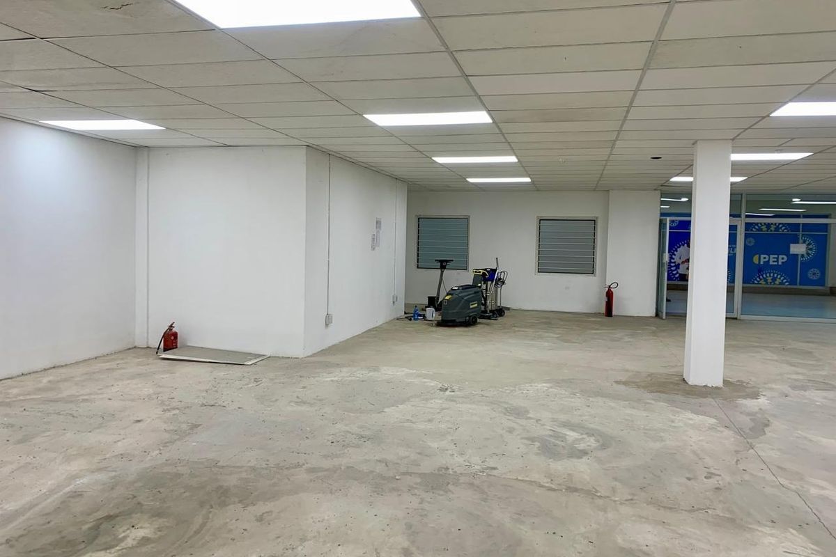 An open-plan commercial space featuring a suspended ceiling with recessed lighting, structural columns, and unfinished concrete flooring, suitable for retail or office fit-out.