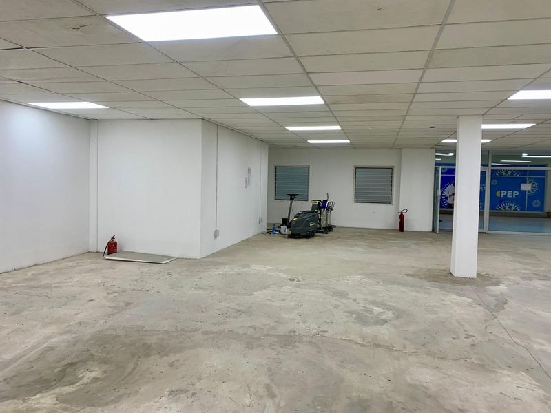 An open-plan commercial space featuring a suspended ceiling with recessed lighting, structural columns, and unfinished concrete flooring, suitable for retail or office fit-out.