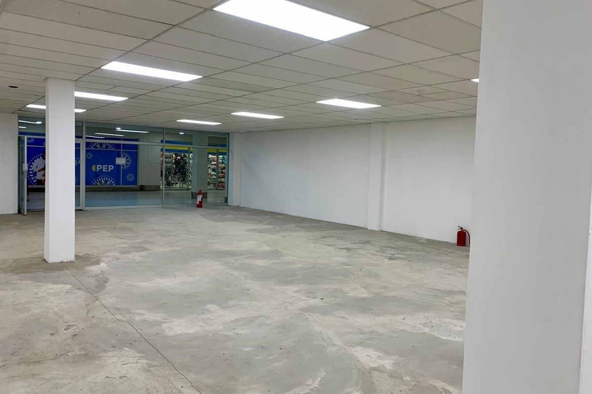 An empty commercial open-plan retail space featuring a suspended ceiling, recessed lighting, and a concrete floor with a glass storefront entrance.