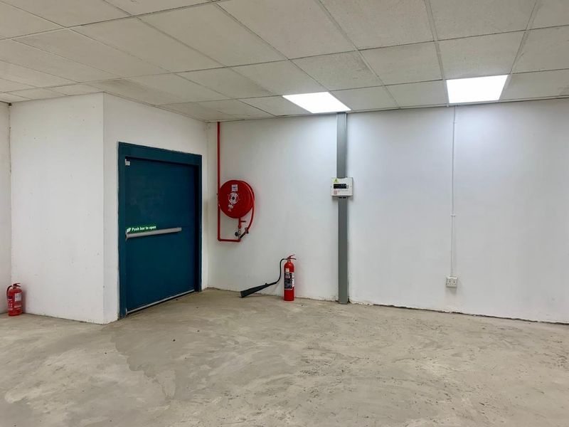 A functional utility space featuring an emergency exit door, fire safety equipment, and a suspended ceiling with recessed lighting.