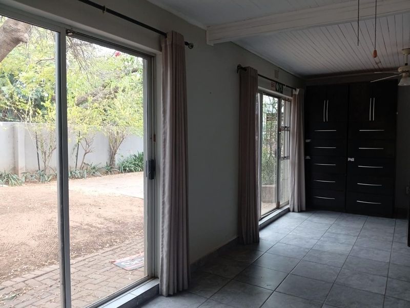 A bright, empty office space featuring tiled flooring, built-in storage cabinetry, and large sliding glass doors providing direct access to the outdoor area.