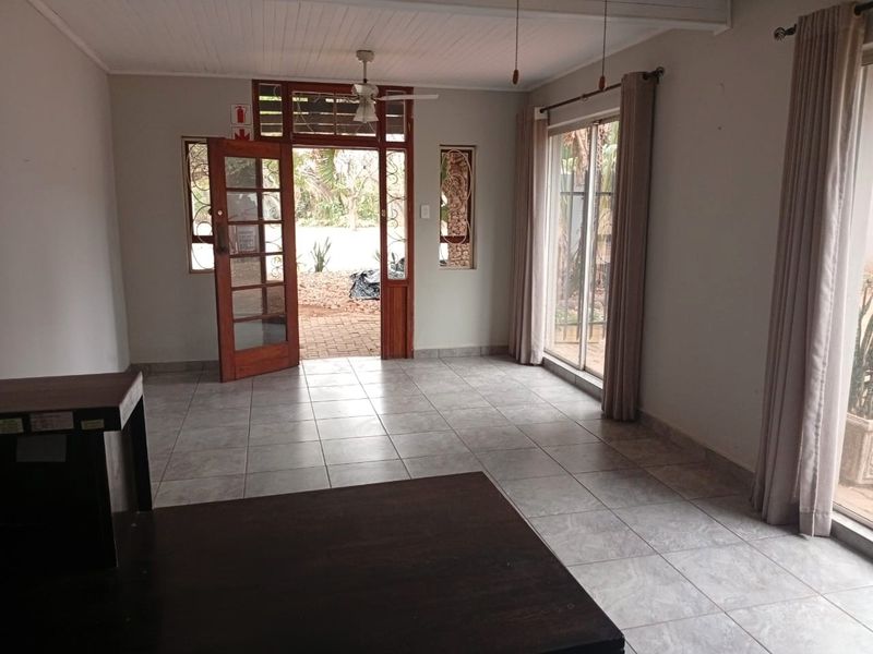 A bright, tiled entrance area featuring a timber-framed glass door, sliding glass doors, and a ceiling fan, offering direct access to the exterior.