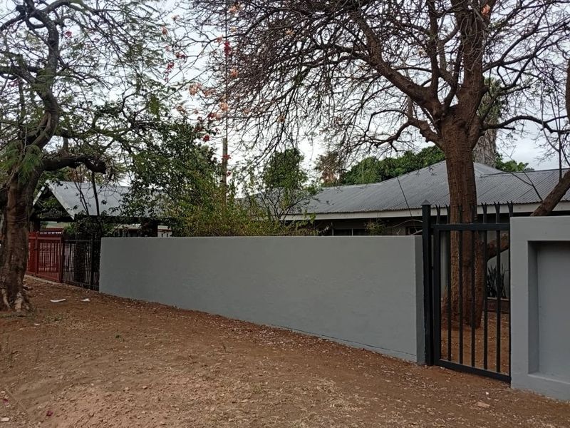 Front view of the office property featuring a grey perimeter wall, metal gate, and corrugated metal roofing.