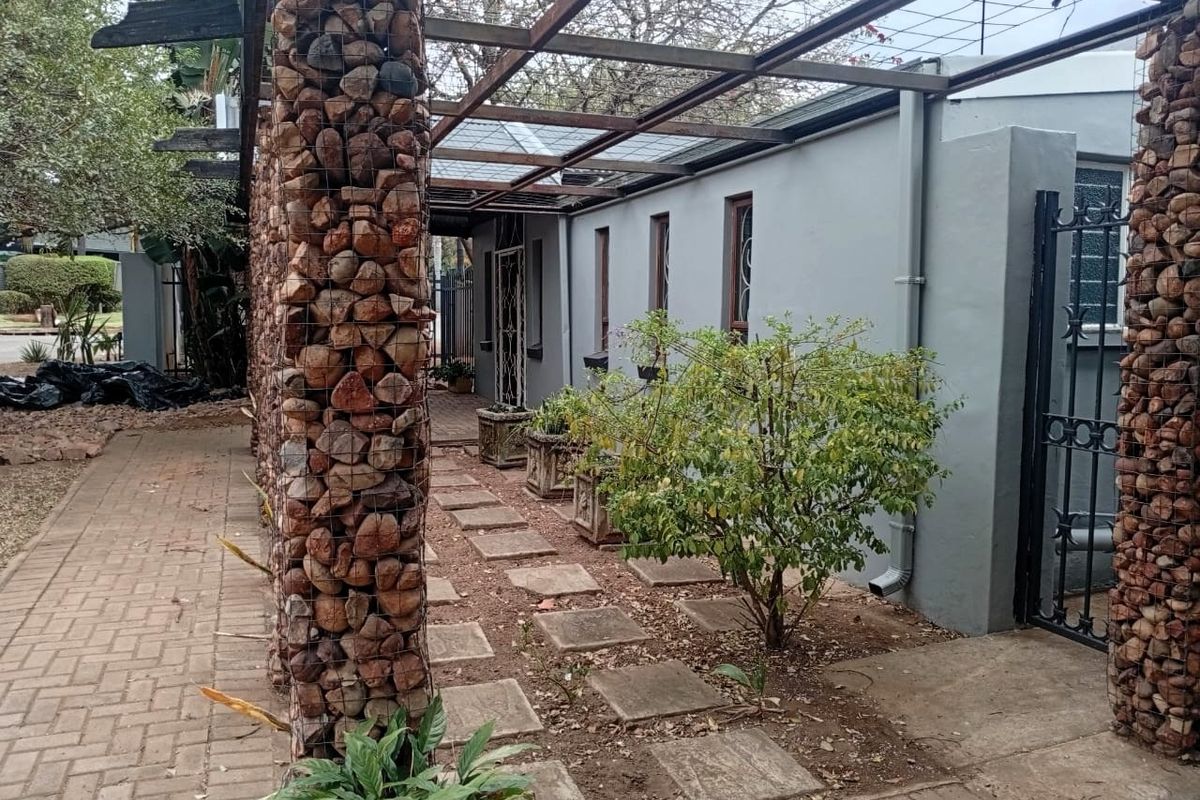 Exterior view of the office property featuring a unique gabion stone pillar pergola structure, paved walkways, and a secure metal gate entrance.
