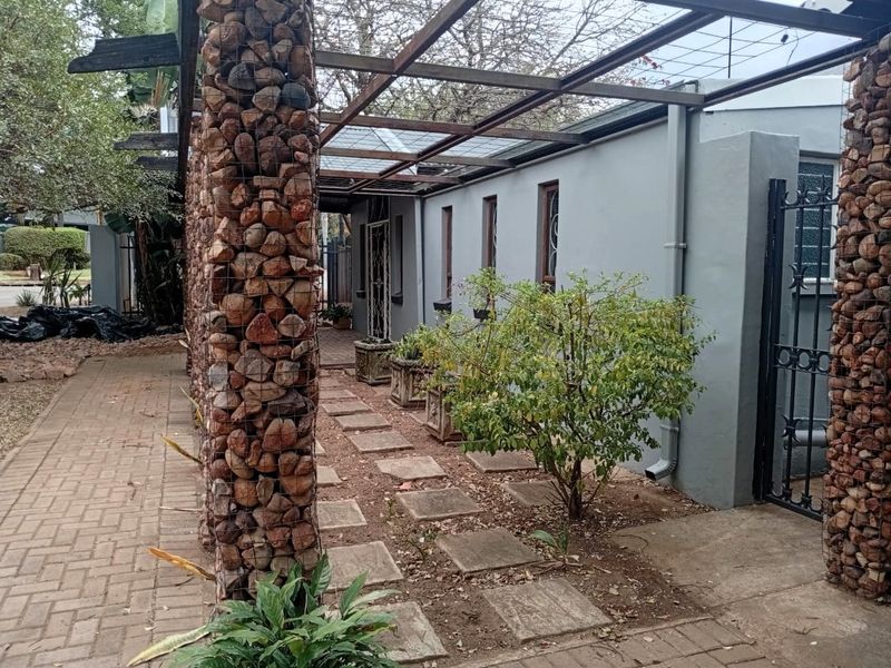 Exterior view of the office property featuring a unique gabion stone pillar pergola structure, paved walkways, and a secure metal gate entrance.