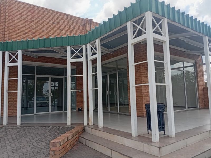 Front exterior view of a retail property featuring a brick facade, glass storefront entrance, and a covered tiled patio area.