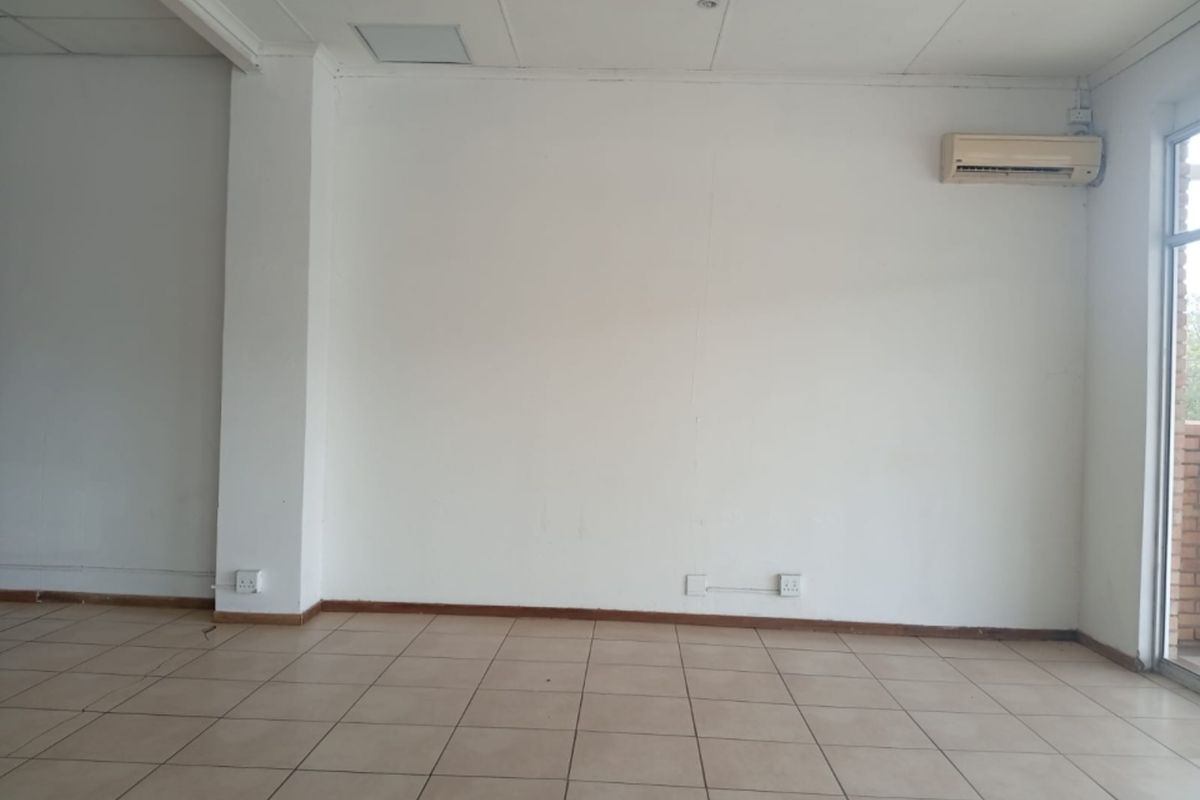 An empty, open-plan retail space featuring tiled flooring, a suspended ceiling, and a wall-mounted air conditioning unit.