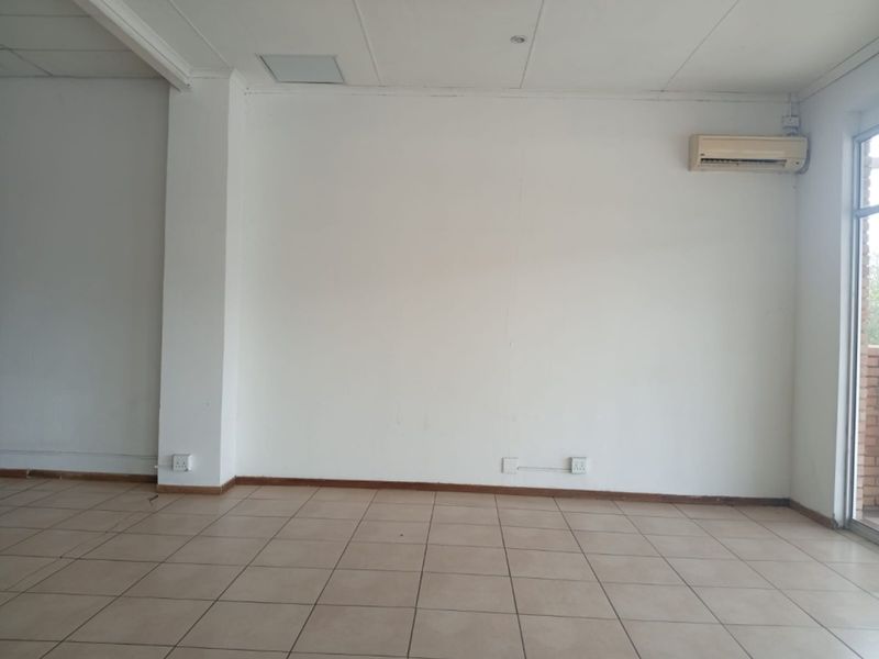 An empty, open-plan retail space featuring tiled flooring, a suspended ceiling, and a wall-mounted air conditioning unit.