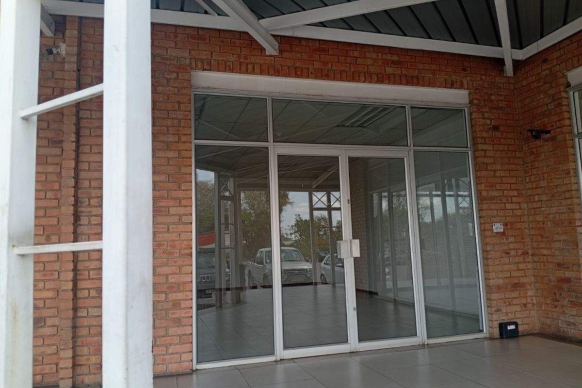 Front entrance of a retail space featuring an exposed brick facade, large glass storefront, and a covered tiled patio area.