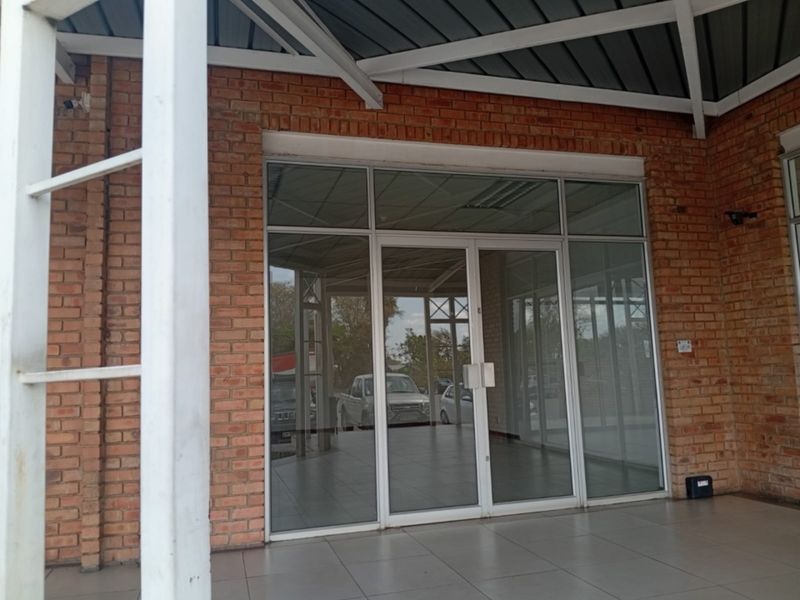 Front entrance of a retail space featuring an exposed brick facade, large glass storefront, and a covered tiled patio area.