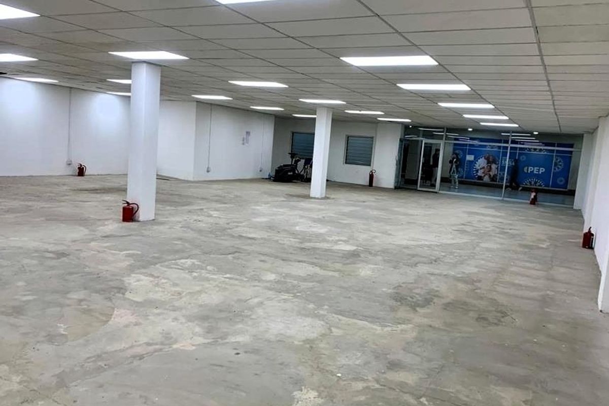 A large, open-plan retail space featuring a suspended ceiling with recessed lighting, structural columns, and a glass storefront entrance, currently in shell condition.