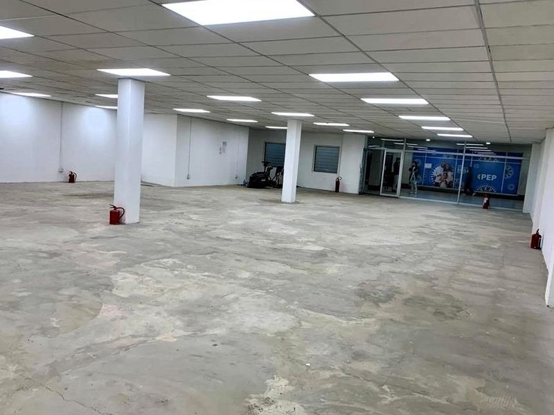 A large, open-plan retail space featuring a suspended ceiling with recessed lighting, structural columns, and a glass storefront entrance, currently in shell condition.