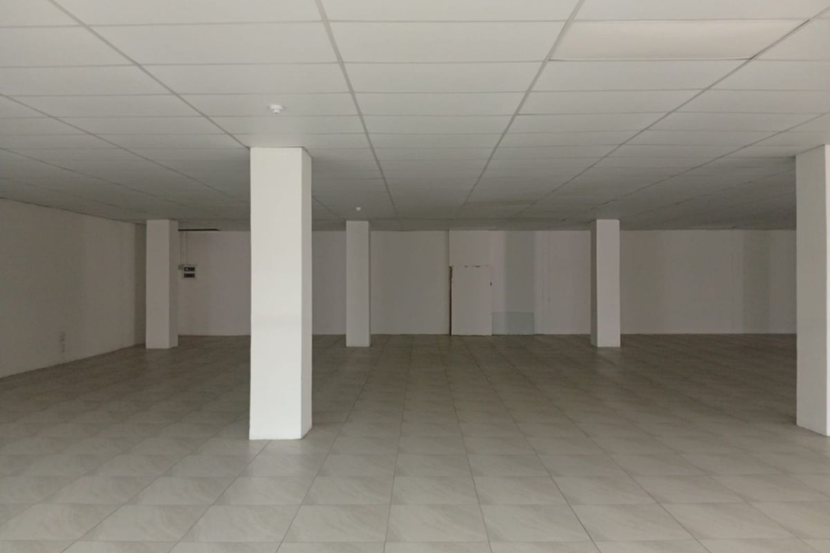 A spacious, empty open-plan retail area featuring neutral tiled flooring, a suspended ceiling, and structural support columns throughout the interior space.