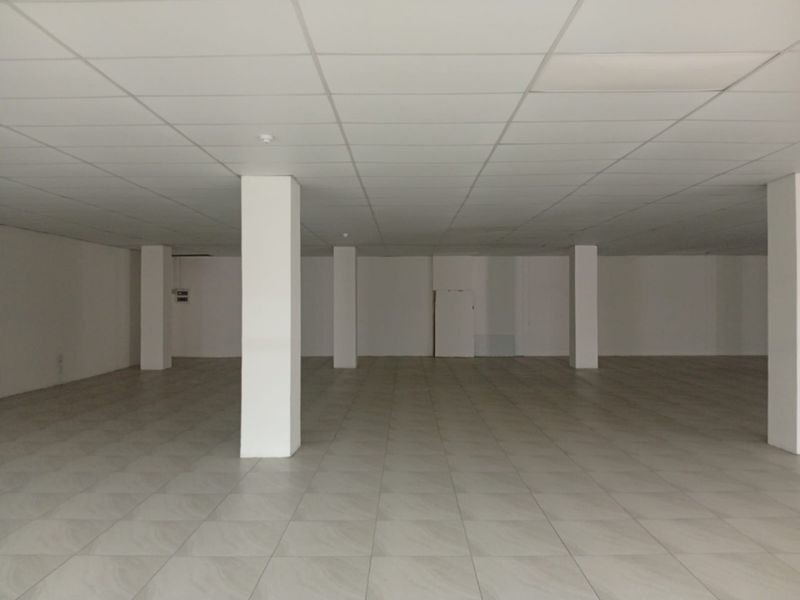 A spacious, empty open-plan retail area featuring neutral tiled flooring, a suspended ceiling, and structural support columns throughout the interior space.