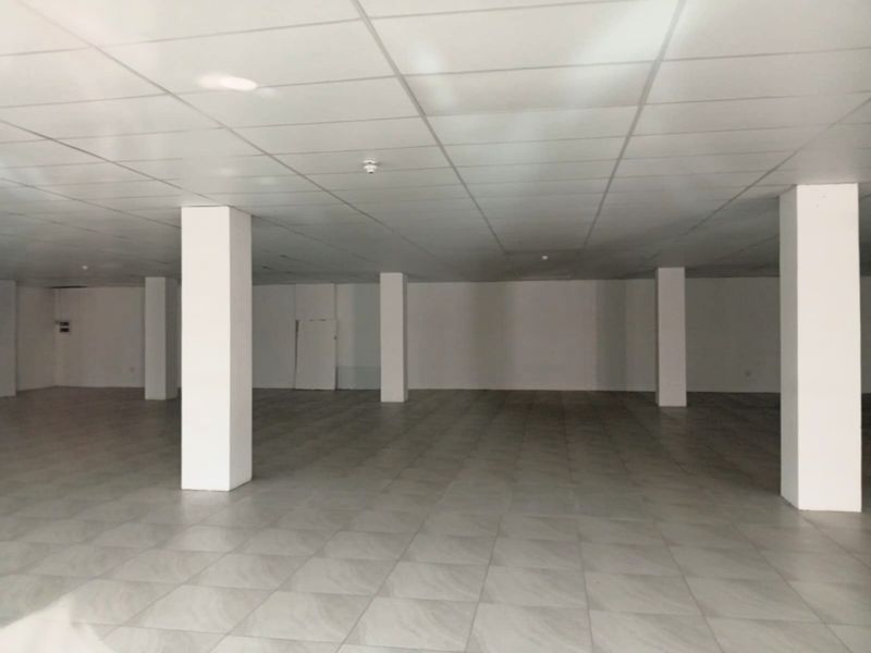 A spacious, open-plan retail area featuring a clean suspended ceiling, neutral tiled flooring, and structural support columns, ready for custom fit-out.