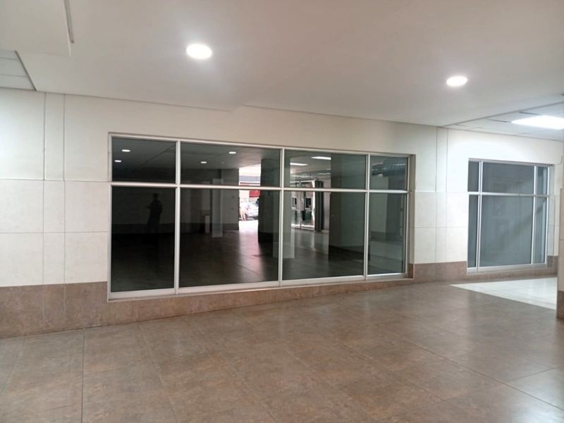 A vacant retail space featuring large glass storefront windows, recessed ceiling lighting, and neutral tiled flooring, suitable for various commercial business applications.