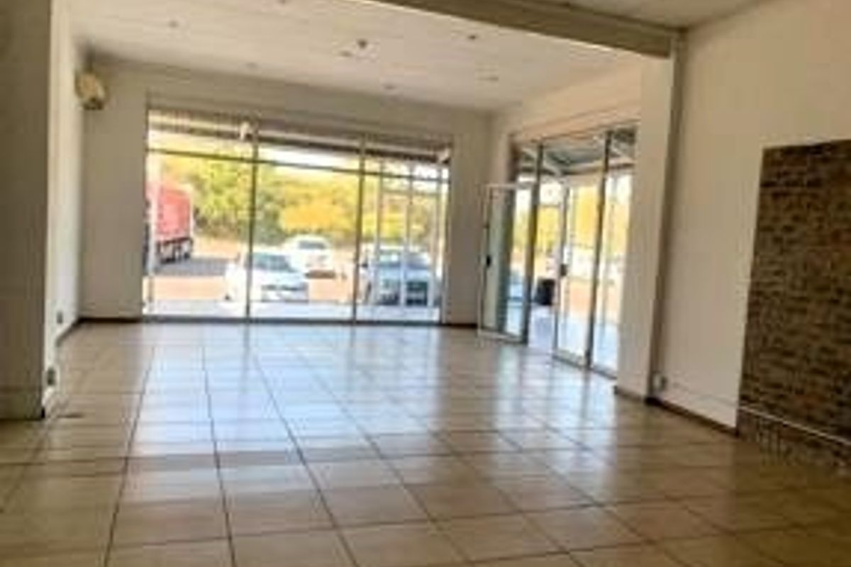 Spacious open-plan retail unit featuring large glass storefront windows, tiled flooring, and an exposed brick feature wall, offering excellent natural light and visibility.