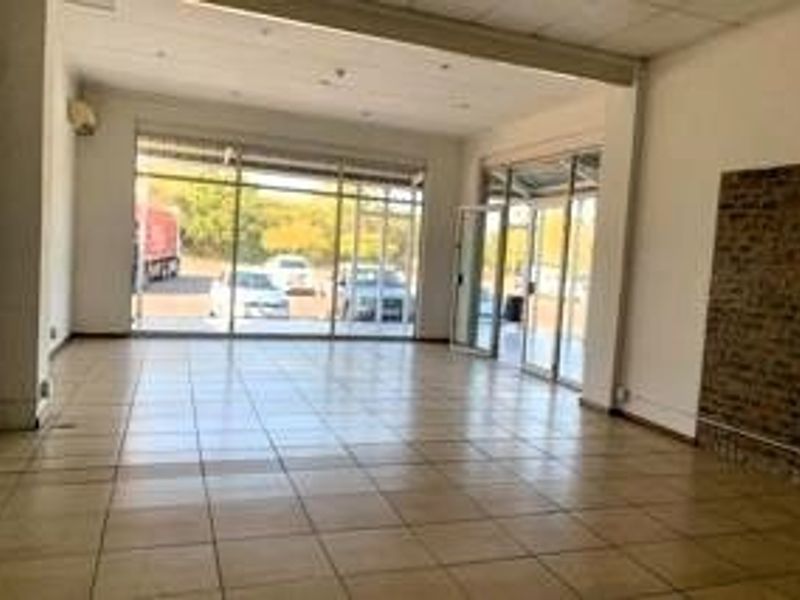 Spacious open-plan retail unit featuring large glass storefront windows, tiled flooring, and an exposed brick feature wall, offering excellent natural light and visibility.
