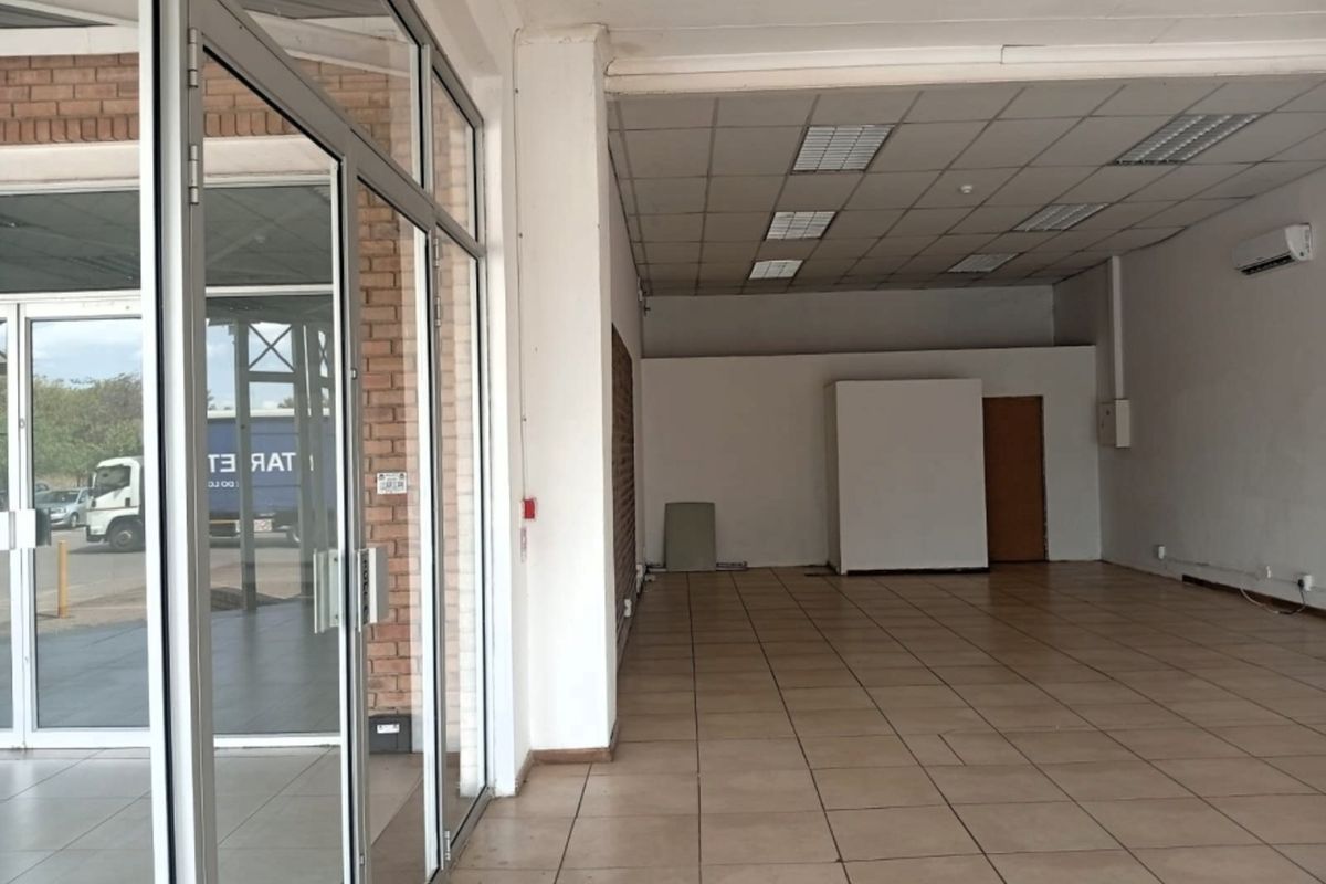 Spacious open-plan retail unit featuring tiled flooring, a suspended ceiling with recessed lighting, and a large glass storefront entrance.