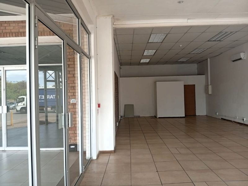 Spacious open-plan retail unit featuring tiled flooring, a suspended ceiling with recessed lighting, and a large glass storefront entrance.