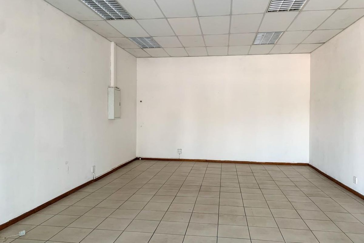 An empty commercial office space featuring neutral ceramic floor tiles, a suspended ceiling with recessed lighting, and clean white walls.