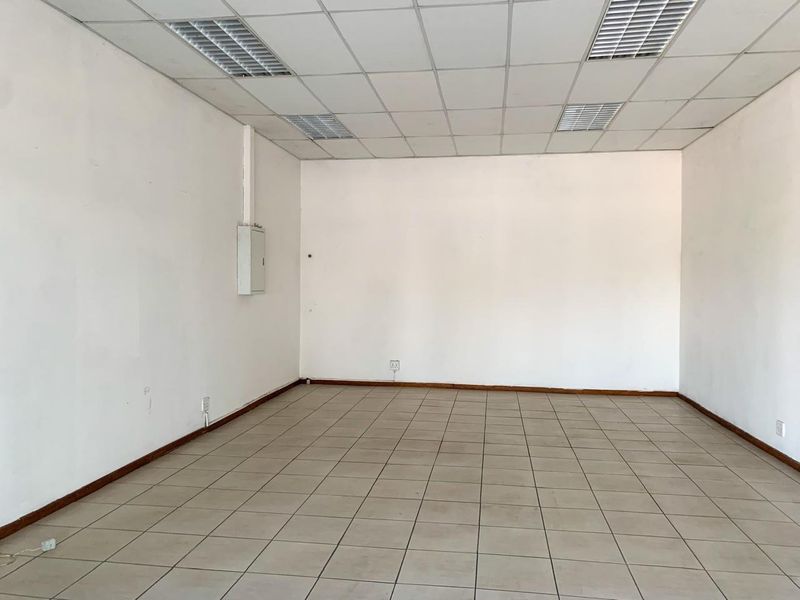 An empty commercial office space featuring neutral ceramic floor tiles, a suspended ceiling with recessed lighting, and clean white walls.