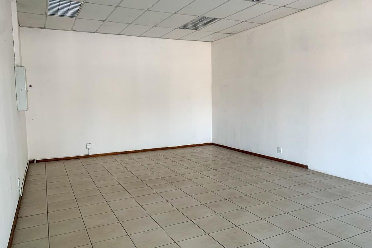 An empty commercial office space featuring neutral ceramic floor tiles, a suspended ceiling with recessed lighting, and clean white walls.