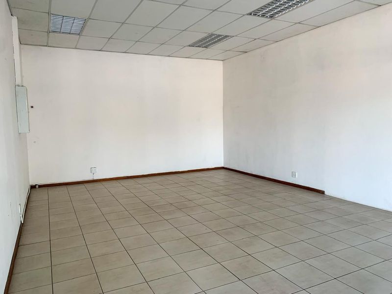An empty commercial office space featuring neutral ceramic floor tiles, a suspended ceiling with recessed lighting, and clean white walls.