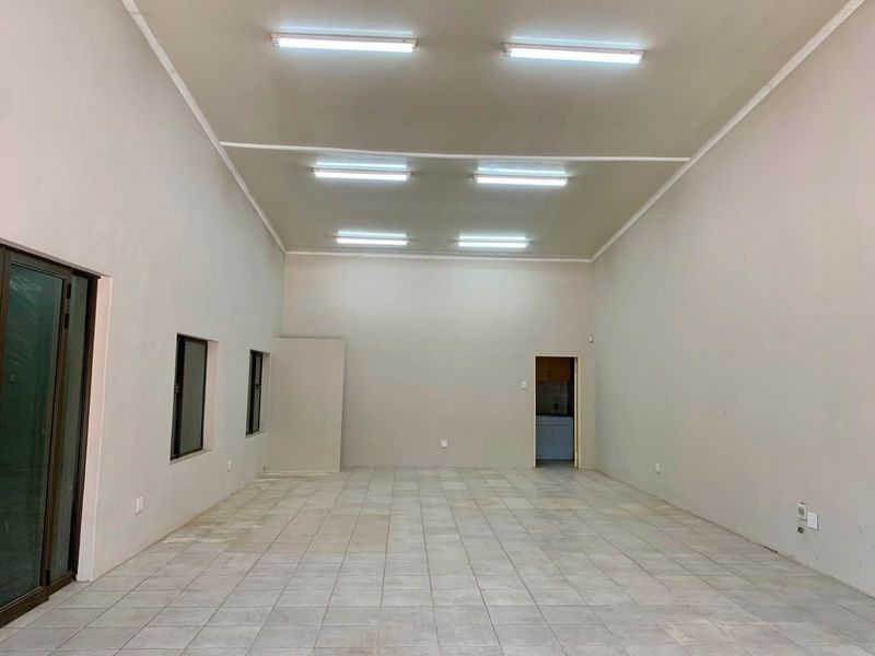 A spacious, empty office area featuring neutral walls, tiled flooring, and overhead fluorescent lighting, providing a versatile blank canvas for professional use.