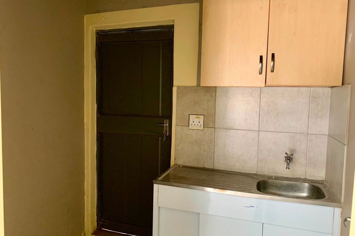 A compact kitchenette featuring a stainless steel sink, tiled splashback, and overhead cabinetry, suitable for a small office utility space.