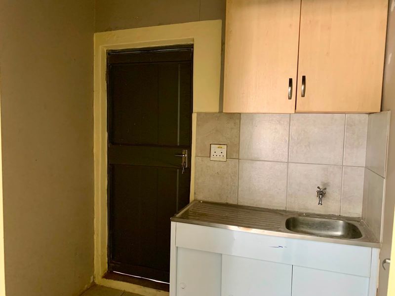 A compact kitchenette featuring a stainless steel sink, tiled splashback, and overhead cabinetry, suitable for a small office utility space.