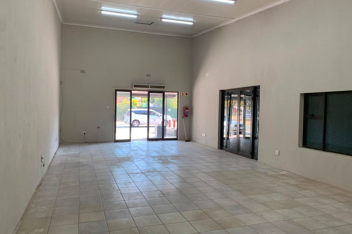 A spacious, empty office unit featuring tiled flooring, fluorescent lighting, and large glass entrance doors, providing a clean canvas for professional use.