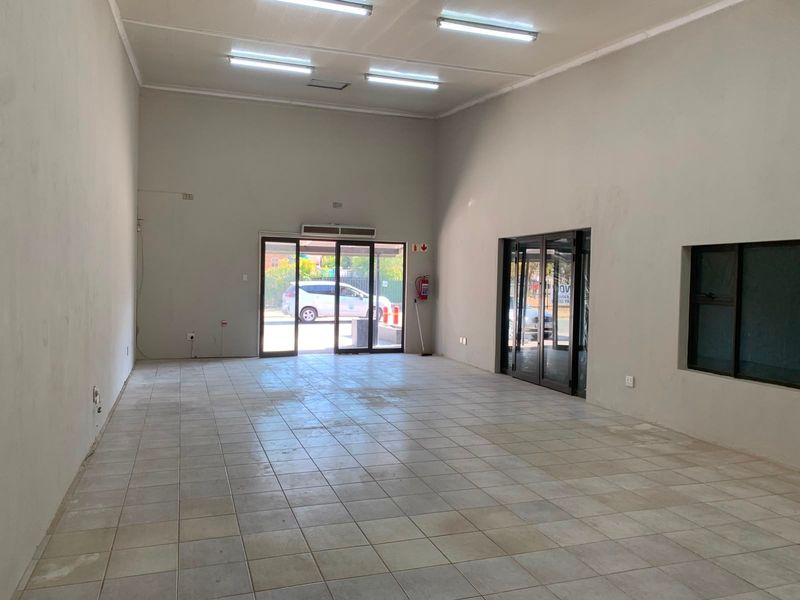A spacious, empty office unit featuring tiled flooring, fluorescent lighting, and large glass entrance doors, providing a clean canvas for professional use.