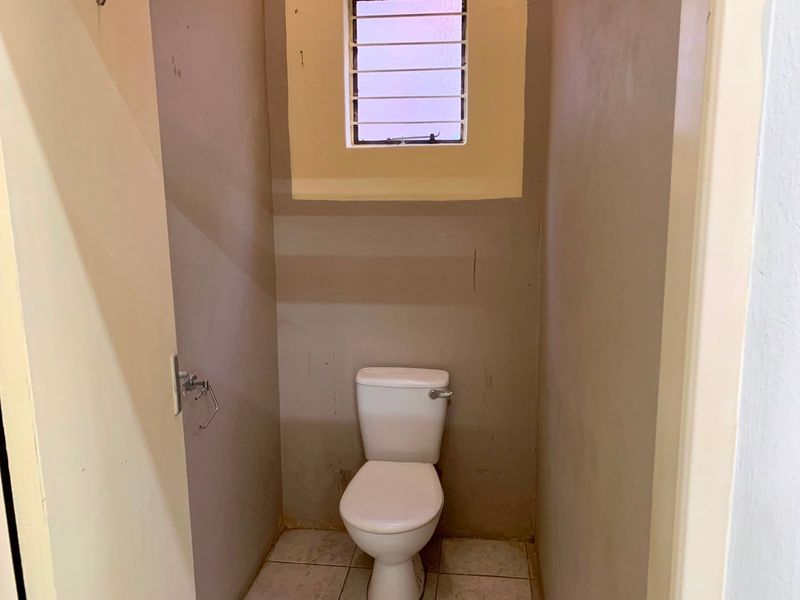A small, functional restroom featuring a standard toilet, tiled flooring, and a high-set window with security bars.