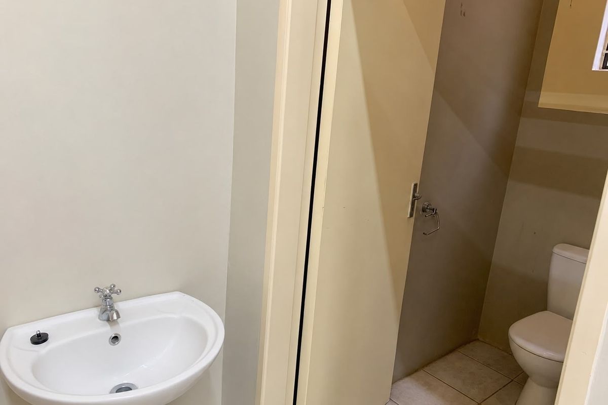 A functional office bathroom featuring a pedestal washbasin and a separate toilet cubicle with tiled flooring.