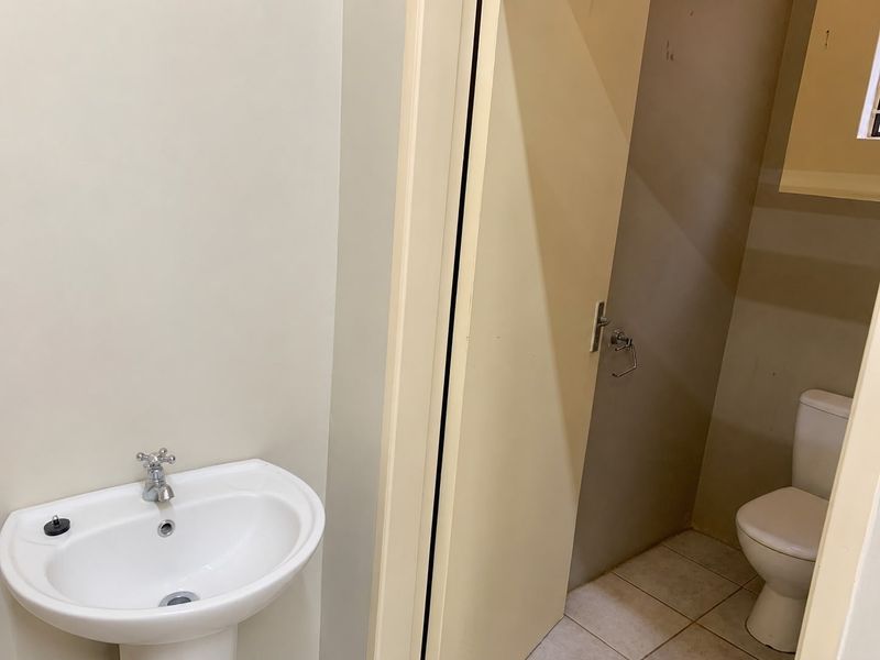 A functional office bathroom featuring a pedestal washbasin and a separate toilet cubicle with tiled flooring.