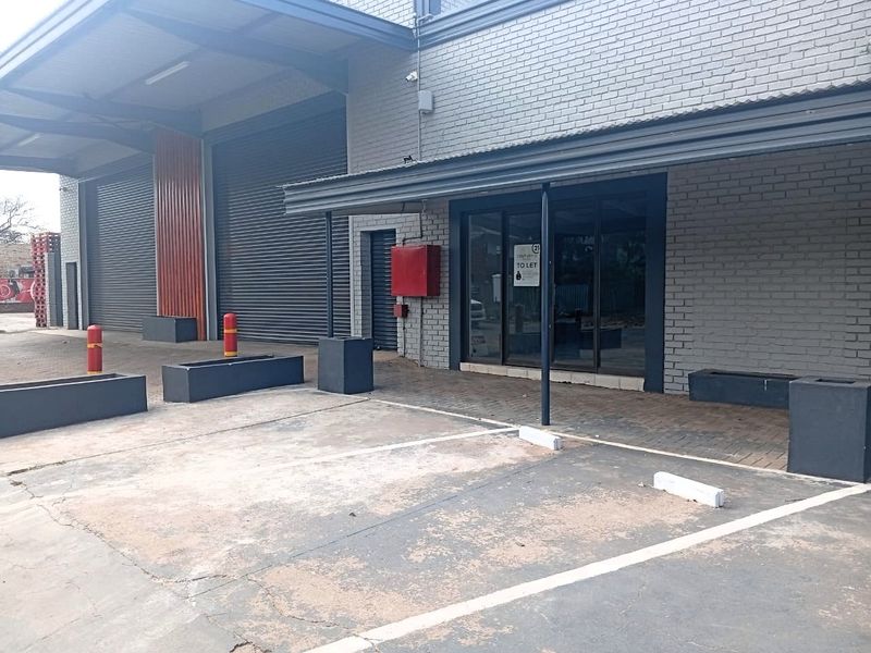 Front exterior view of an industrial office property featuring roller shutter doors, a covered entrance, and dedicated paved parking bays.