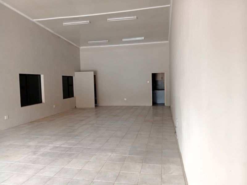 A spacious, empty office area featuring neutral wall finishes, tiled flooring, and integrated fluorescent lighting, suitable for a professional workspace layout.