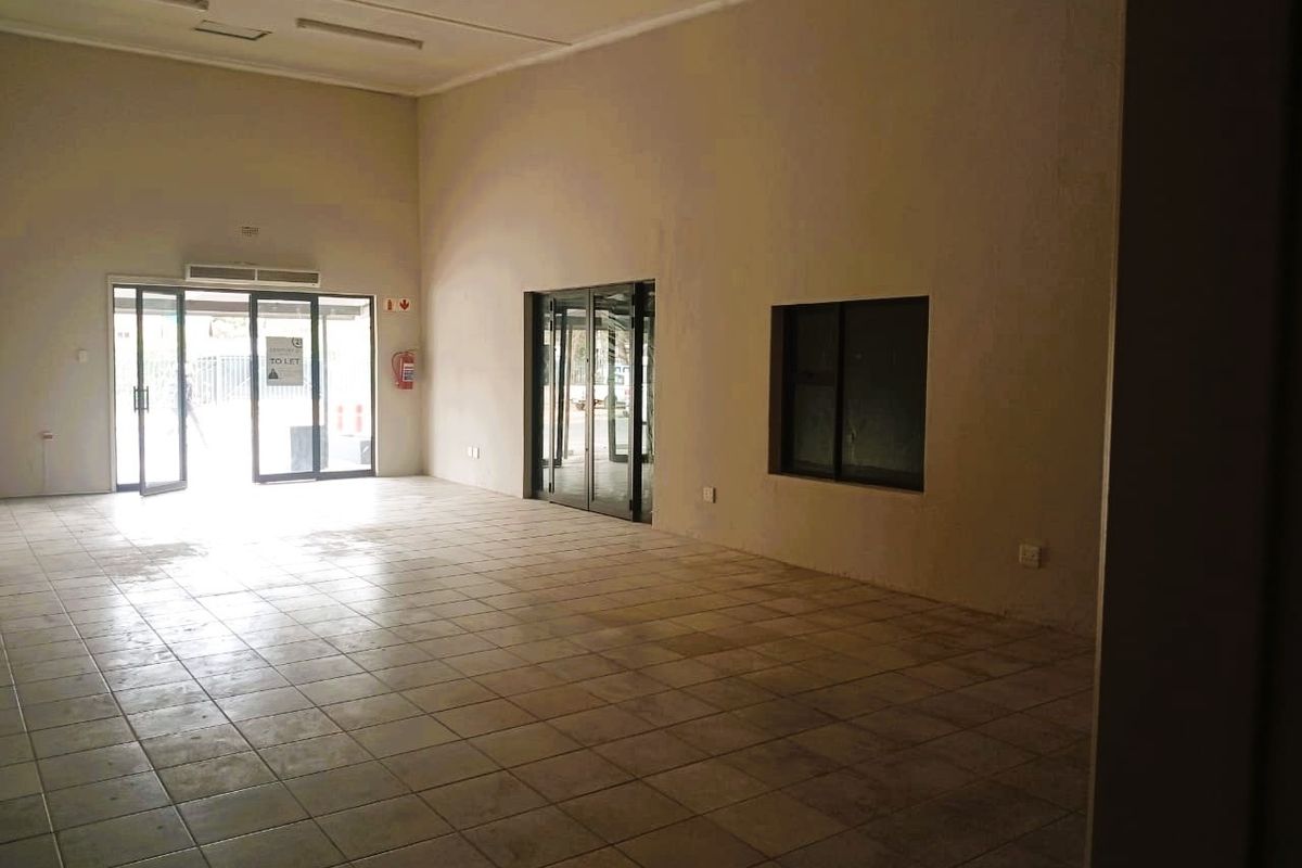 An empty, open-plan office space featuring tiled flooring, recessed ceiling lights, and glass entrance doors, suitable for a variety of commercial uses.