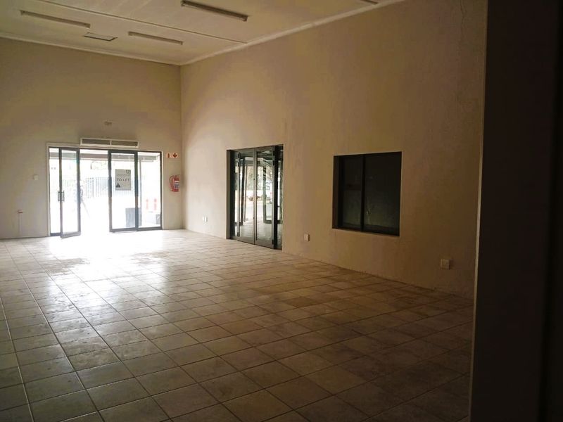 An empty, open-plan office space featuring tiled flooring, recessed ceiling lights, and glass entrance doors, suitable for a variety of commercial uses.