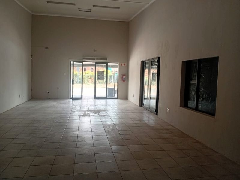 An empty, open-plan office space featuring tiled flooring, glass entrance doors, and wall-mounted air conditioning, suitable for a variety of commercial business uses.