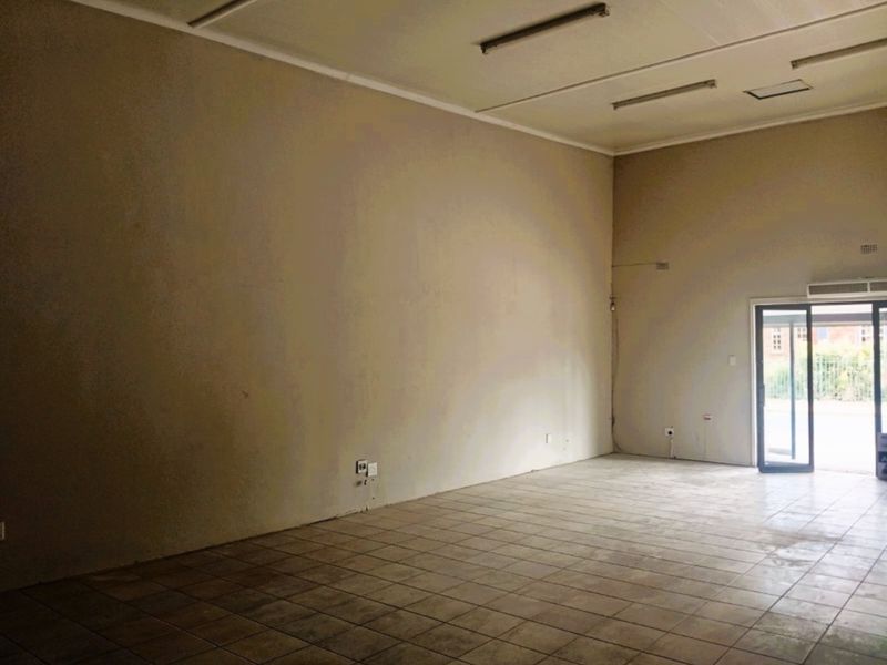 A spacious, empty office unit featuring tiled flooring, fluorescent lighting, and a glass panel entrance door, offering a blank canvas for professional use.