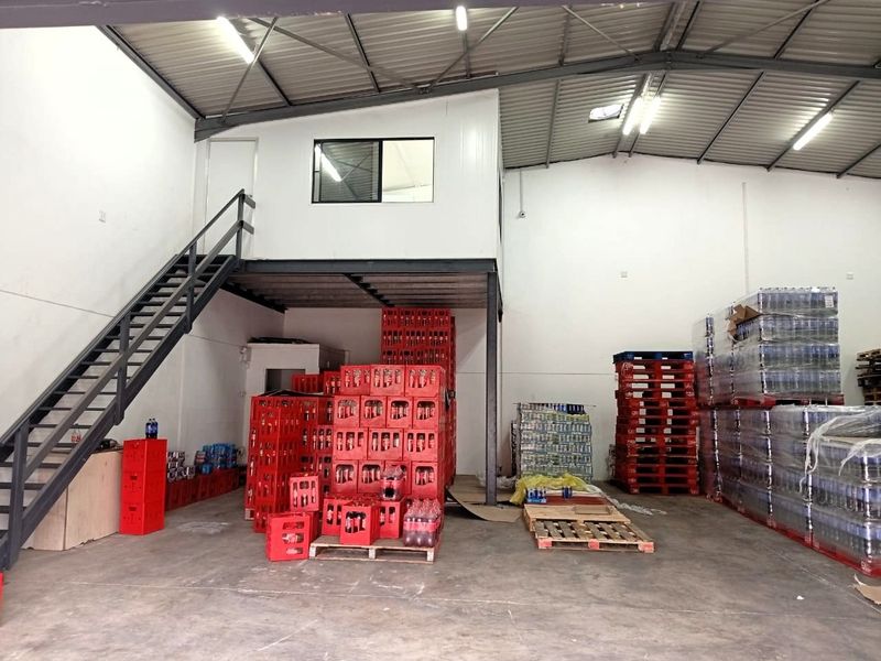 Industrial warehouse space featuring a mezzanine level with metal staircase access, high ceilings with exposed steel trusses, and durable concrete flooring.