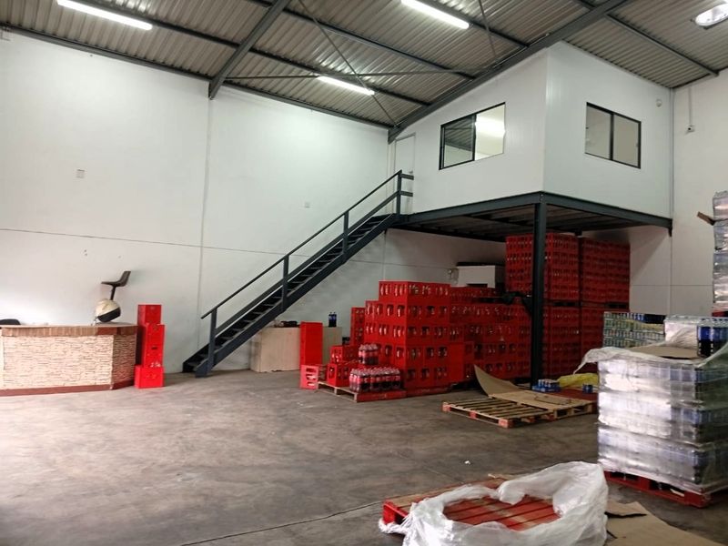Industrial warehouse space featuring a mezzanine level with steel staircase, exposed roof trusses, and concrete flooring, suitable for storage or operational use.